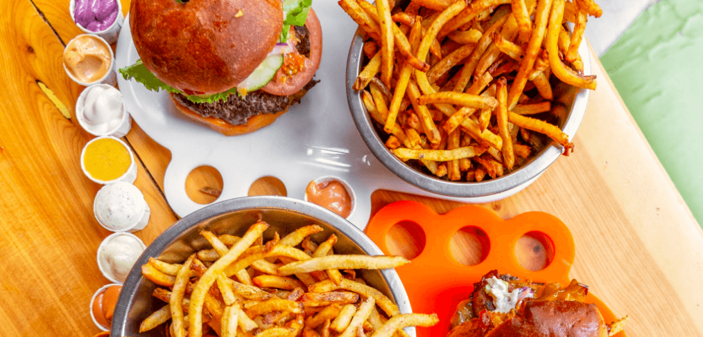 top view of two burgers and two bowls of fries on a wooden table